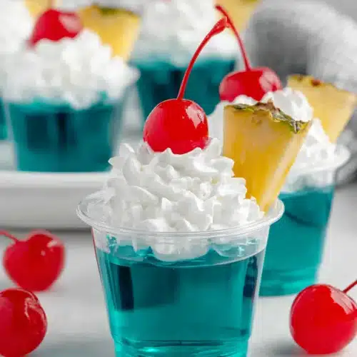 Blue Hawaiian jello shots with whipped cream, cherry, and pineapple garnish