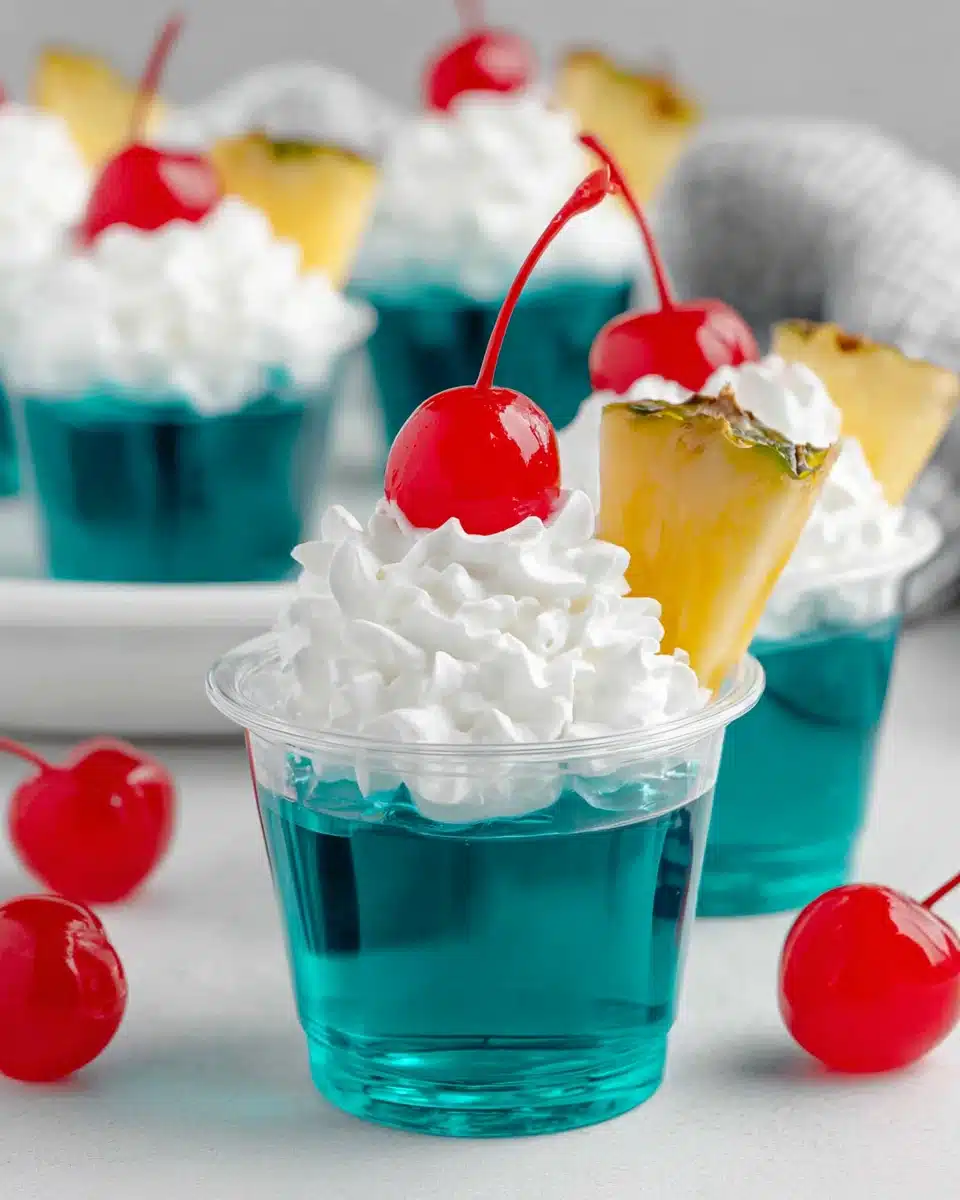 Blue Hawaiian jello shots with whipped cream, cherry, and pineapple garnish