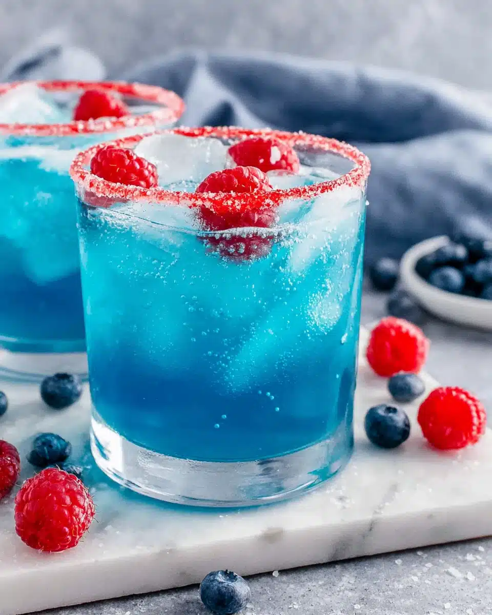 Blue Hawaiian Lemonade Punch in glasses with raspberry garnish and red sugared rims