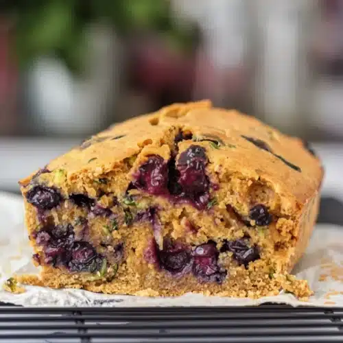 Moist blueberry zucchini bread with visible berries and zucchini, cooling on a rack