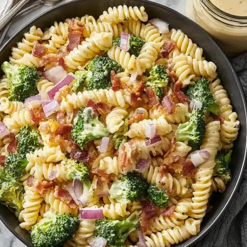 Broccoli pasta salad with rotini, broccoli, bacon, and red onion in a dark bowl