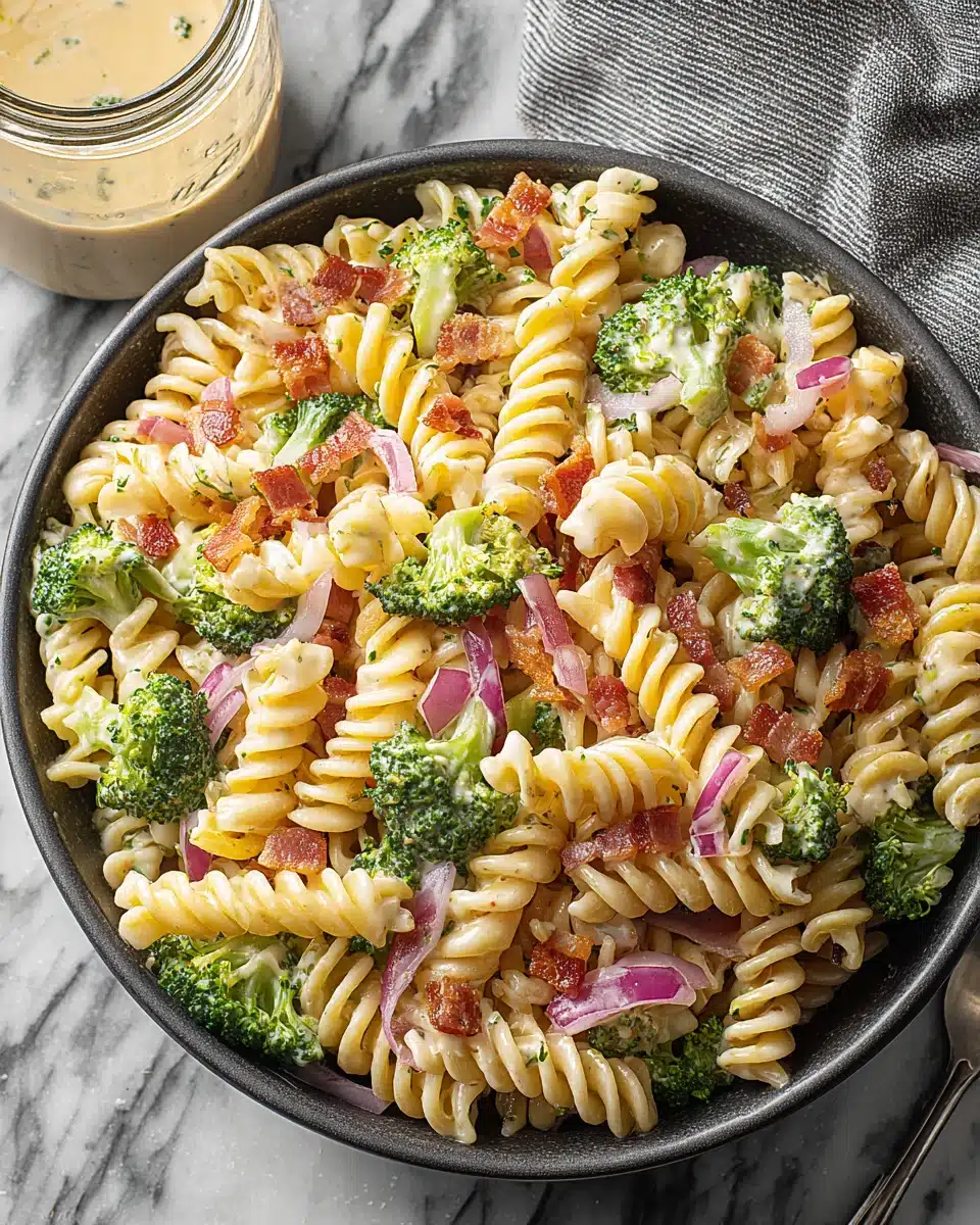 Broccoli pasta salad with rotini, bacon, and red onions in a creamy dressing