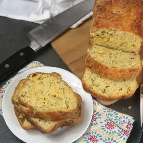 Sliced cheddar garlic herb keto bread on a plate with knife and cutting board