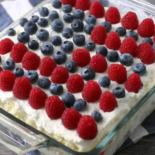 Easy flag cake with red raspberries and blueberries arranged like the American flag on a creamy white base.