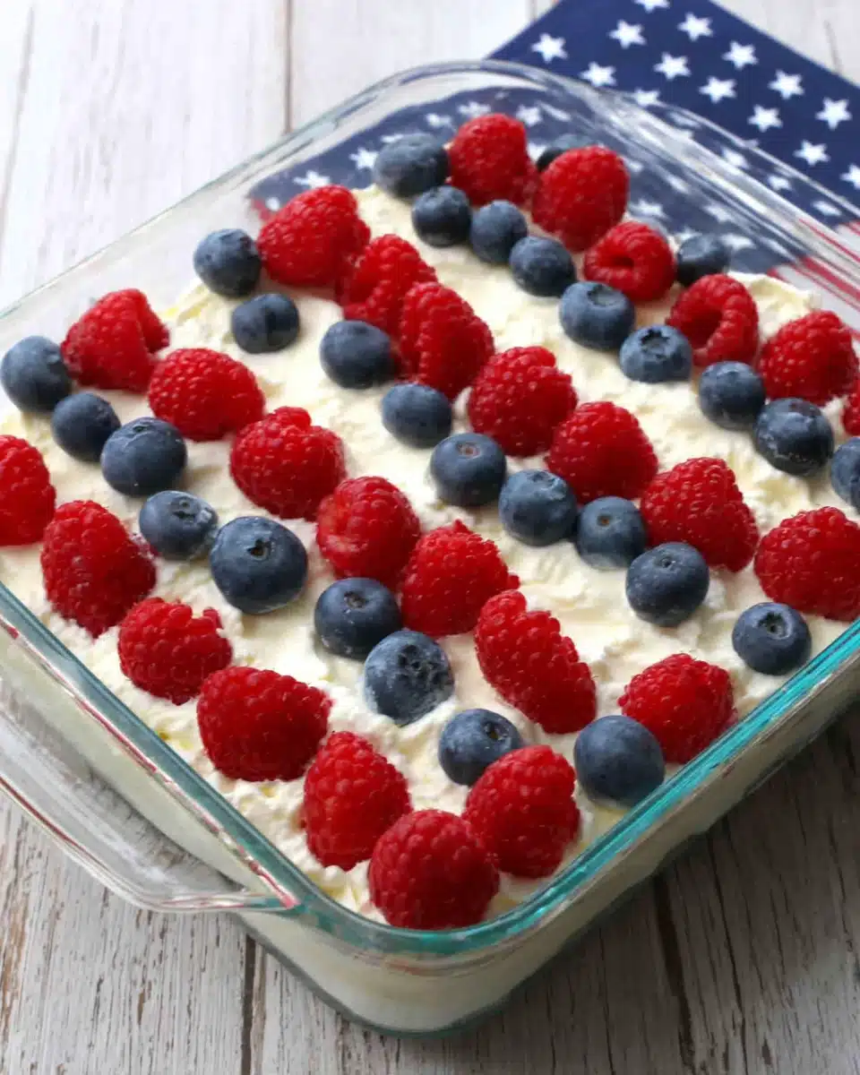 Easy flag cake with red raspberries and blueberries arranged like the American flag on a creamy white base.