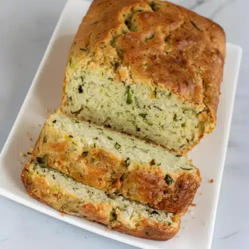 Ina Garten zucchini bread sliced on a white plate, showing moist texture and green zucchini bits