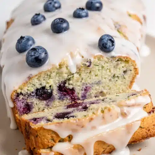 Keto lemon blueberry zucchini bread with glaze and fresh blueberries on wooden board