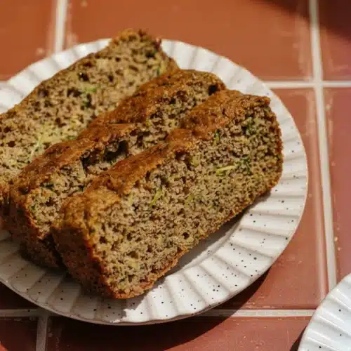 Slices of keto zucchini bread on a white plate with visible zucchini and nuts