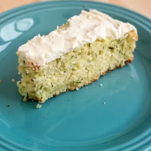 A slice of lemon cucumber cake with frosting on a teal plate