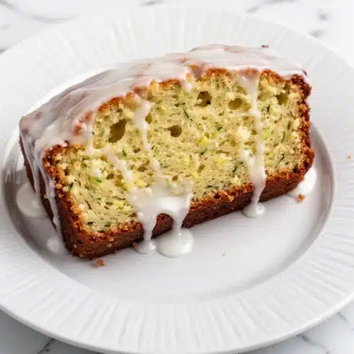 Moist lemon raspberry zucchini bread slice with white glaze on white plate