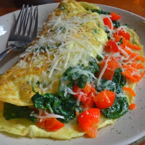 Low carb spinach and cheese omelette with melted cheese and fresh vegetables on a plate