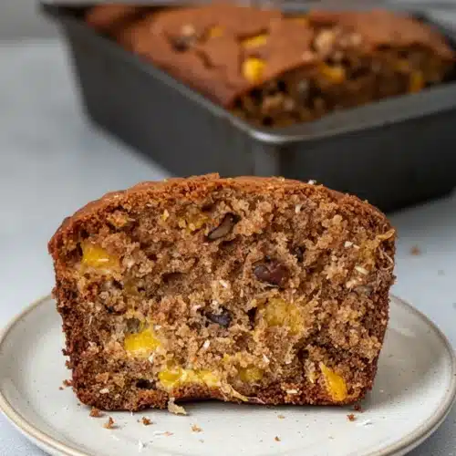 Moist mango bread slice with visible mango chunks and walnuts, held in hand