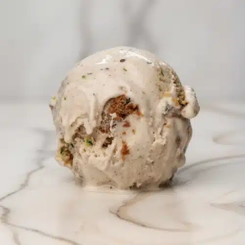 Moist spiced zucchini bread ice cream swirl with crumbles, creamy texture, white marble background