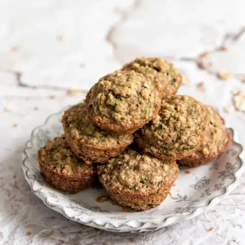 Oatmeal zucchini muffins stacked on a white plate with shredded zucchini in the background
