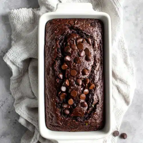 One bowl gluten free chocolate zucchini bread in a white loaf pan with chocolate chips on top
