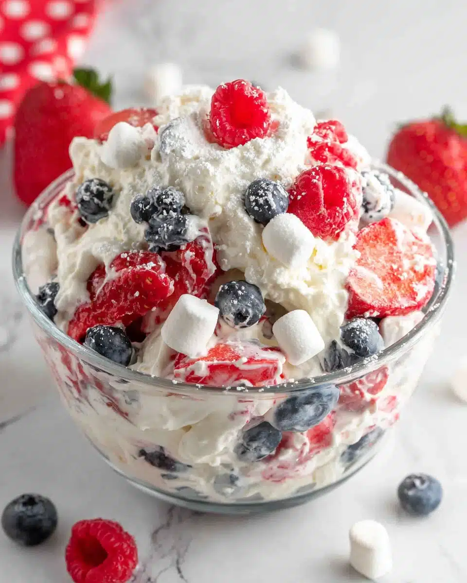 Red white and blue cheesecake salad with strawberries, blueberries, and marshmallows in a glass bowl