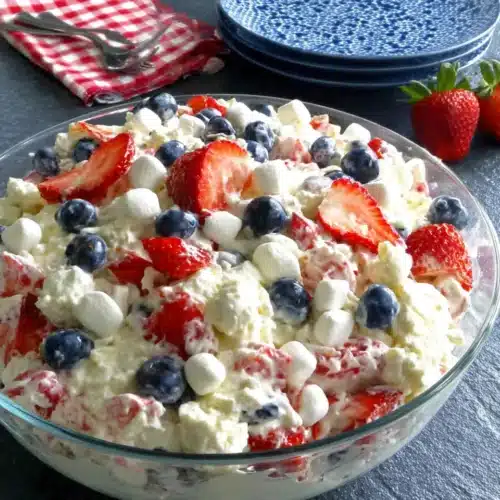 Red, white & blue cheesecake salad with strawberries, blueberries, and marshmallows in a glass dish