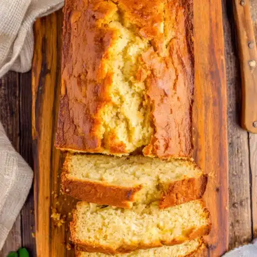 Sliced southern peach bread on a wooden board with a bowl of cream nearby