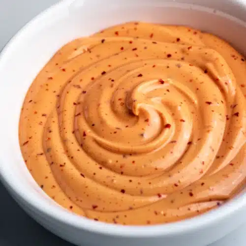 Creamy spicy mayo with red chili specks in a white bowl