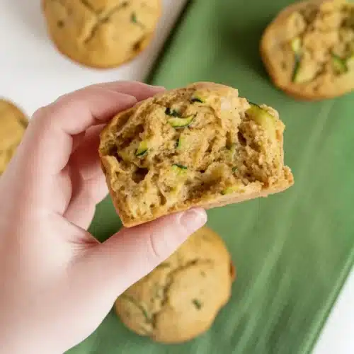 Baby-friendly zucchini muffin held in hand, showing moist texture and green flecks