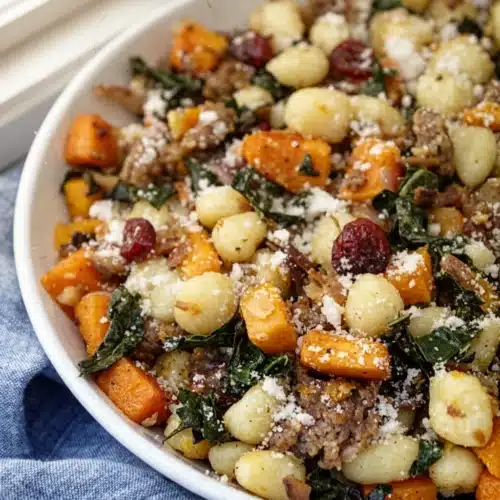 Butternut squash sausage gnocchi with kale and cranberries in a white bowl