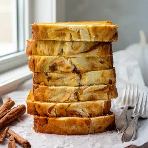Cream cheese stuffed pumpkin bread slices stacked on a wooden board with cinnamon sticks