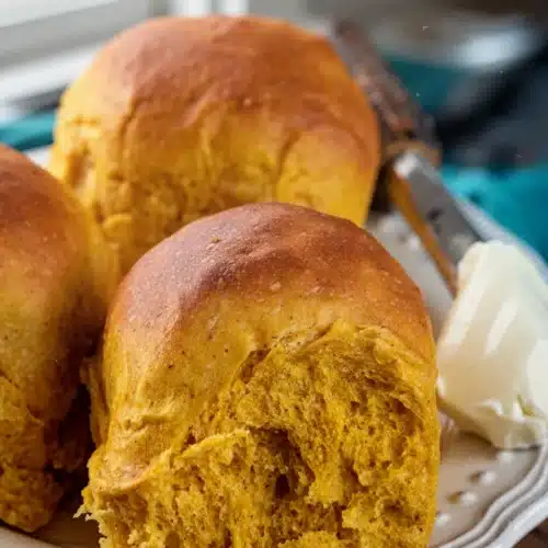 Fluffy pumpkin sourdough dinner rolls with butter on a white plate