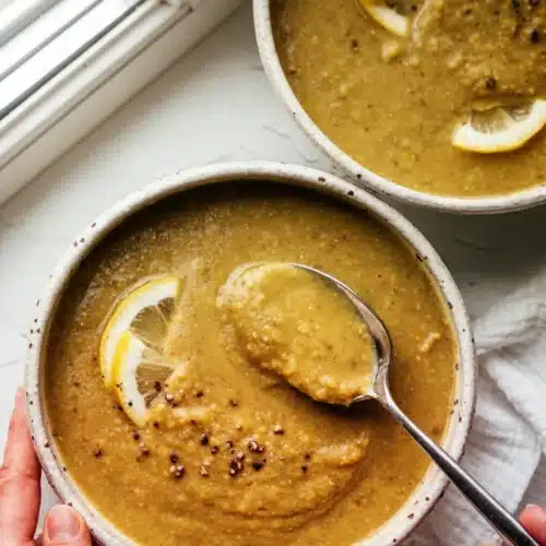 Creamy lemony lentil soup in white bowls with lemon garnish
