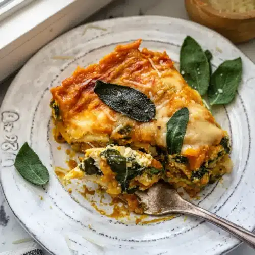 Vegetarian pumpkin spinach lasagna slice on a plate with sage leaves