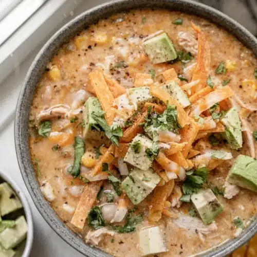 Creamy white chicken chili in a bowl with avocado, tortilla strips, and cilantro, garnished with lime